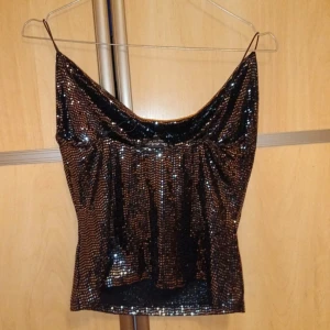 Svart glittrig tubtopp - Snygg svart tubtopp med glittrande paljetter. Perfekt för festliga tillfällen med en elegant och iögonfallande design.