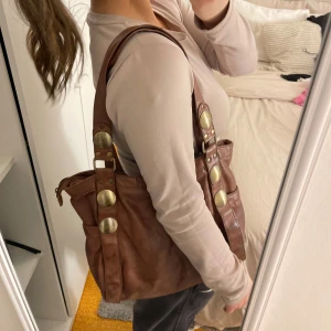 Brun axelväska med leopardmönstrat foder - Snygg brun axelväska i skinn med stora dekorativa knappar. Insidan har ett coolt leopardmönstrat foder och en praktisk innerficka med dragkedja. Perfekt för skolan eller för en touch till din outfit🥰