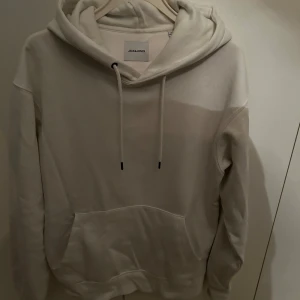 Beige hoodie från Jack & Jones - Säljer en stilren vit hoodie från Jack & Jones. Den har en klassisk design med en stor ficka framtill och justerbar huva med dragsko. Perfekt för en avslappnad look. Köpt i betyg för 599.