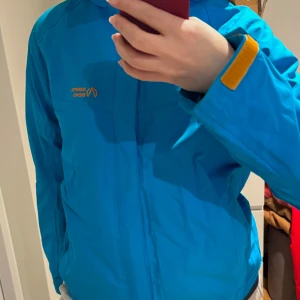 Blå vindjacka från North Bend - Snygg blå vindjacka från North Bend med orangea detaljer. Jackan har en dragkedja framtill.