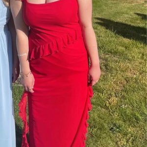 Röd balklänning med volangdetaljer - Snygg röd långklänning med volangdetaljer längs sidan. Klänningen har använts en gång på balen och är perfekt för ett liknande tillfälle. Annars bara till en sommarkväll på picknick. 