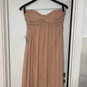 Aprikosrosa balklänning  - Säljer en elegant ljusrosa axelbandslös klänning från NLY Trend. Den är helt oanvänd och har fortfarande lappen kvar. Om du är intresserad så är det bara att skriva så ska jag fixa fler bilder och försöka svara på frågor. Den är perfekt för finare evenemang. För mig som är 179cm var längden rätt bra. 