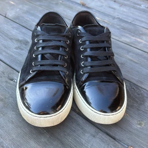 Svarta Lanvins - Snygga svarta sneakers från Lanvin med glansig tå och snörning. Skorna har en vit sula och är perfekta för en stilren look.