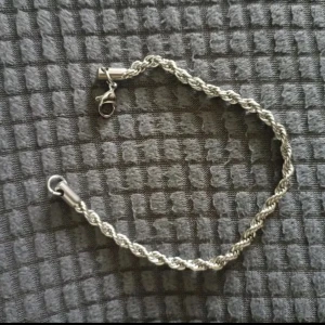 Rostfri stål armband i tvinnad design - Snyggt silverfärgat armband med en elegant tvinnad design. Perfekt för att ge en stilren touch till din outfit. Armbandet har en praktisk låsmekanism som gör det enkelt att ta på och av.