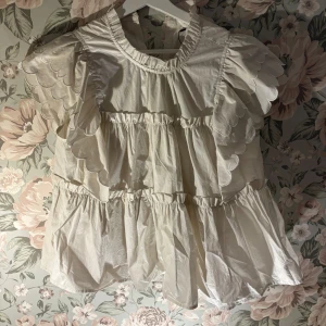 Vit blus med volangdetaljer - Charmig vit blus med volangdetaljer och korta ärmar. Blusen har en luftig passform och är perfekt för vår och sommar. Aldrig använd och prislappen är kvar, ny pris 700kr☺️