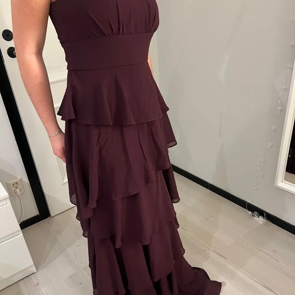 Elegant vinröd axelbandslös klänning med flera lager volanger som ger en vacker rörelse. Perfekt för speciella tillfällen. Klänningen har en dragkedja i ryggen för enkel påklädning. Aldrig använd och prislappen är kvar, storlek S!💗. Mekot.
