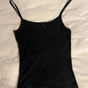 Linne med spets och rosett - Fint och knappt använt svart linne från H&M. Jättegulligt med spets runt kanten och en rosett i mitten! Storlek XS☺️