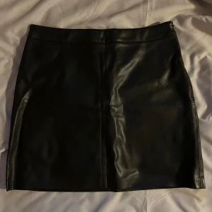 Svart skinnkjol från Gina Tricot - Snygg svart skinnkjol från Gina Tricot i storlek 38. Kjolen har en stilren design med en kort längd som passar perfekt för en trendig look. Tillverkad i ett glansigt material som ger en lyxig känsla. Finns en mindre ”skada” se sista bilden. 