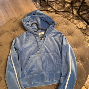 Blå velour hoodie från Juicy Couture - Säljer en blå velour hoodie från Juicy Couture me. Den har vita ränder längs ärmarna och texten 'Juicy' i strass på ryggen. Använd några få gånger äkta såklart 