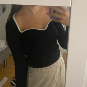 Svart långärmad topp med vit kant - Snygg svart långärmad topp med  vit kant runt halsringningen. Från hm