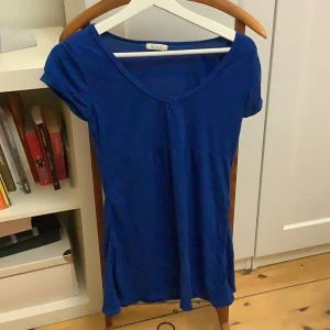 Blå topp från Cubus - Säljer en blå topp från Cubus i storlek M. Toppen har en v-ringad design och korta ärmar, perfekt för en avslappnad stil. Tillverkad i ett mjukt material som känns skönt mot huden.