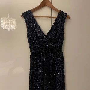Mörkblå paljettklänning från Meet Me There - Snygg mörkblå klänning täckt av glittriga paljetter från Meet Me There. Klänningen har en v-ringad design och är ärmlös, perfekt för en festlig kväll. Aldrig använd.