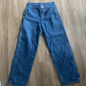 Blå jeans med drakbroderi - Snygga blå jeans med ett coolt drakbroderi i guld på baksidan. Byxorna har en rak passform och hög midja, vilket ger en avslappnad och trendig look. Perfekta för dig som vill sticka ut med en unik detalj.