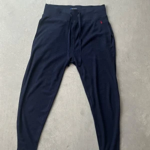 Mörkblå mjukisbyxor från Ralph Lauren - Snygga mörkblå mjukisbyxor från Ralph Lauren med röd broderad logga. Byxorna har en ribbad struktur och snörning i midjan för bästa passform. Perfekta för en avslappnad stil. Använd några få gånger. Inköpt för 700 kr för ca 1 år sedan