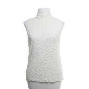 Vit spetsblus från Stockh LM - Elegant vit spetsblus från Stockh LM med hög krage och ärmlös design. Blusen har ett vackert broderat mönster och en dragkedja i ryggen för enkel påklädning. Perfekt för en stilren look.