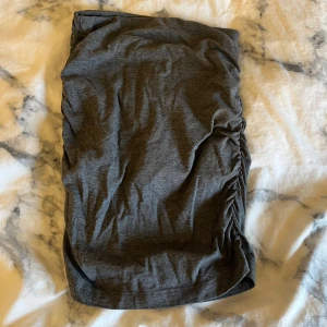 Grå kjol med rynkdetaljer - Snygg grå kjol med rynkdetaljer på sidorna. Kjolen har en tight passform och är gjord i ett mjukt material. 