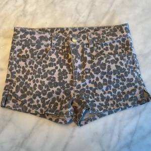 Grå leopardmönstrade shorts från H&M - Snygga grå shorts med leopardmönster från H&M. De har en knapp och dragkedja framtill samt fickor både fram och bak. Perfekta för en trendig look!