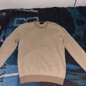 Beige mönstrad tröja från Bruun & Stengade - Säljer en stilren stickad beige tröja från Bruun & Stengade med ett diskret mönster. Tröjan har långa ärmar och ribbade muddar vid ärmslut och nederkant. Perfekt för en avslappnad look. Den är riktigt fet och najs beige färg. Väldigt skön och inte så använd!🫡