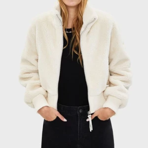 Beige teddyjacka med dragkedja - Mysig beige teddyjacka med dragkedja framtill. Jackan har en avslappnad passform och långa ärmar, perfekt för kyligare dagar. Den är liten i storleken! Den är både stilren och bekväm, vilket gör den till ett måste i garderoben.