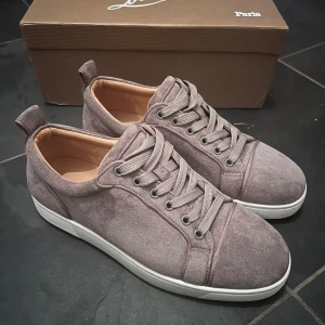 Grå sneakers från Christian Louboutin - Snygga grå sneakers i mocka från Christian Louboutin med den ikoniska röda sulan. Skorna har snörning och en stilren design som passar perfekt för en trendig look. De har en vit sula som kontrasterar snyggt mot det grå mockamaterialet.