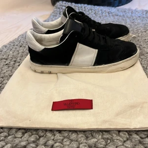 Valentino flycrew  - Snygga Valentino sneakers i svart och vitt med klassisk design. Skorna har snörning och en vit sula med dekorativa nitar baktill. Perfekta för en stilren look. 3 nitar borta mockan är som ny däremot sulan har lossnat från lite här och där på båda skorna kan säkert fixa det pris kan diskuteras.