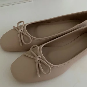 Beige ballerinaskor med rosett - Säljer ett par stilrena beige ballerinaskor med en söt rosett framtill. Skorna är i storlek 39 (6 UK), stora i storlek så passar en 40. Köpta på Vinted, men från Asos. Jättefint skick.