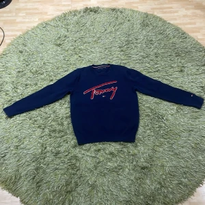 Mörkblå tröja från Tommy Hilfiger - Säljer en snygg mörkblå tröja från Tommy Hilfiger med röd broderad logga på framsidan. Tröjan har långa ärmar och ribbstickad halsringning. Perfekt för en stilren look.