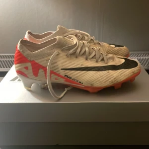 Nike Mercurial fotbollsskor - Säljer ett par Nike Mercurial fotbollsskor i vit med svarta och röda detaljer. Skorna har snörning och är designade för optimal prestanda på planen. Perfekta för dig som vill ha stil och funktion i ett.