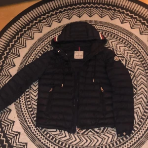 Svart dunjacka från Moncler - Snygg mörkblå dunjacka från Moncler perfekt nu inför våren/vinter. Modellen är storlek 2/M men kan även passa dig som har 1/S. Den är i mycket bra skick! Priset kan gå ner vid snabb affär!