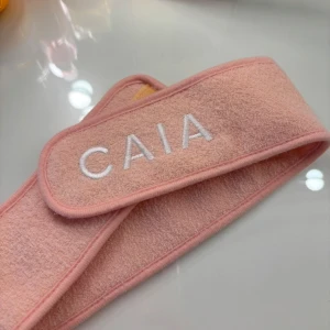 Rosa diadem från CAIA - Säljer ett mjukt rosa diadem från CAIA. Perfekt för att hålla håret borta vid sminkning eller hudvård. Diademet har en enkel design med broderad logotyp i vitt. Använt en gång!