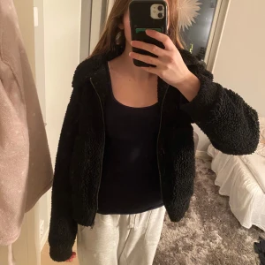 Svart teddyjacka - Svart teddy jacka som är köpt på Gekås Ullared🫶har ett ganska stort hål på insidan av ena armen men det är inget som syns❤️är använd men ändå i bra skick förutom hålet🫶är i stl 158/164 men passar xs❤️