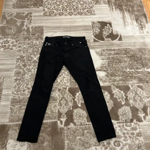 Svarta jeansbyxor från Mavi  - Snygga svarta jeansbyxor med en klassisk femficksdesign från Mavi. De har en dragkedja och knapp framtill. Perfekta för en stilren look.