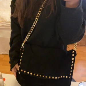 Svart axelväska med nitar - Snygg svart axelväska med guldkedja och coola nitar längs kanterna. Lite defekter vid kedjan men annars jättebra skick! Rymmer mycket får tex plats med tex dator!