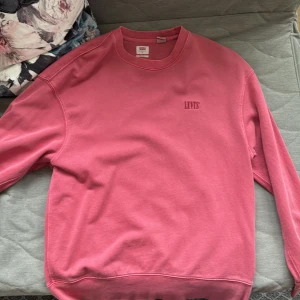 Röd sweatshirt från Levi's - Säljer en snygg rosa sweatshirt från Levi's. Tröjan har en klassisk rund hals och långa ärmar. Perfekt för en avslappnad stil. Levi's-loggan är diskret placerad på bröstet.
