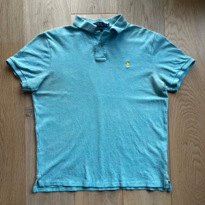 Ljusblå pikétröja från Ralph Lauren - Säljer en stilren ljusblå pikétröja från Ralph Lauren. Tröjan har en klassisk krage med två knappar och det ikoniska broderade logotypen i gult på bröstet. Perfekt för en avslappnad men ändå snygg look. Storlek M, passar även L. Deodorant fläckar i armhålan.