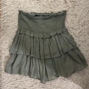 Grön kjol från KappAhl - Säljer en söt grön kjol från KappAhl i storlek XS. Kjolen har en volangdesign med flera lager och en elastisk midja för bekväm passform. Perfekt för en avslappnad stil.