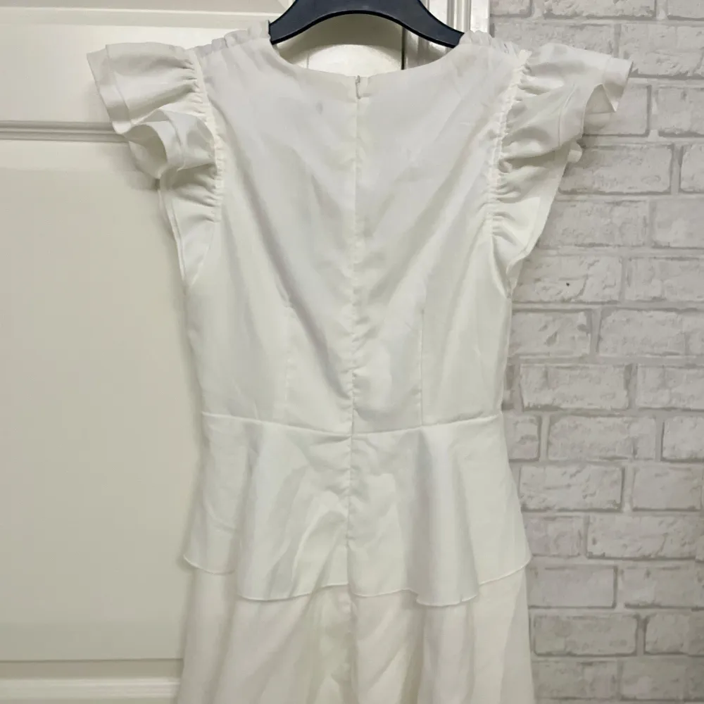 Ny söt vit klänning från Boohoo med volanger och v-ringning. Klänningen är aldrig använd, har korta ärmar och en fin volangdetalj i midjan som ger en lekfull look. Perfekt till midsommar, student eller utomlandsresor🌸. Mekot.