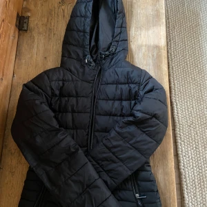 Svart pufferjacka från Zara - Säljer en svart pufferjacka från Zara i mycket bra skick. Jackan har en huva och dragkedja framtill, perfekt för höst och vinter. Den är långärmad och har en normal passform. Supermysig och stilren för kyliga dagar!