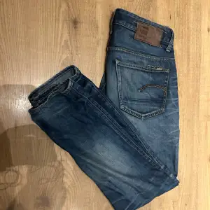 Säljer ett par snygga blå jeans från G-Star RAW med snygga slitningar. Litet hål vid skrevet men går enkelt att sy ihop därav priset