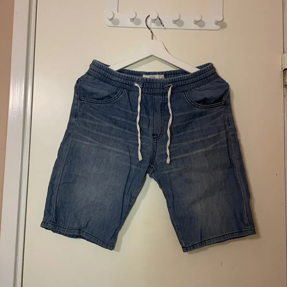 Säljer ett par bekväma blå jeansshorts från Lindex i loose fit. De har elastisk midja med dragsko och två fickor fram och bak. Perfekta för en avslappnad sommarstil! 🩳. Shorts.