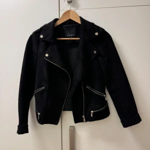 Svart jacka från New Yorker - Säljer en fin svart jacka från New Yorker med dragkedje-detaljer i ”fejk mocka”. Den är använd men i fint skick. Finns en fläck som jag inte fått bort men du som är bra på fläckborttagning kanske kan få bort den! 