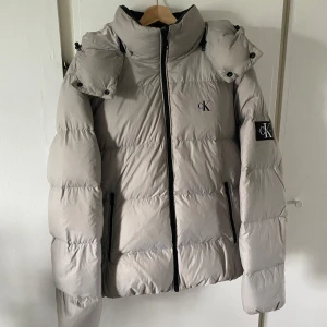 Beige pufferjacka från Calvin Klein L - Säljer en snygg beige pufferjacka från Calvin Klein i bra skick. Perfekt inför kommande vinterkyllan med sin varma och stilrena design. Säljer då jag är sugen på något nytt! Priset är inte hugget i sten.