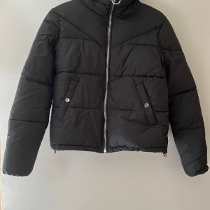 Svart pufferjacka - Säljer en svart pufferjacka i mycket bra skick. Den har en dragkedja framtill och två fickor med knappar. Jackan är perfekt för kalla dagar och har en normal passform, skulle nog även kunna funka till en S. Den är långärmad och riktigt mysig att ha på sig under höst och vinter.