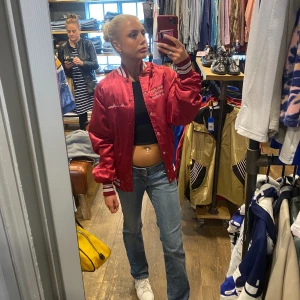 Vintage collegejacka  - Säljer en snygg vintage collegejacka köpt i London i glansigt material. Jackan har vita och röda ribbade muddar vid ärmslut och nederkant. Säker då den inte kommit till användning!