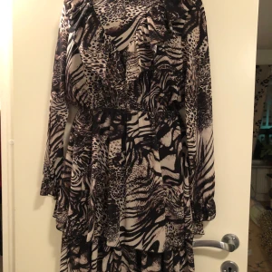 Mönstrad klänning med volanger - Säljer en superfin klänning med djurmönster i svart och beige. Den har långa ärmar och volanger som ger en härlig rörelse. Perfekt för höst och vår, och funkar lika bra till fest som till vardags. Klänningen är i nyskick och har en normal passform. 🖤