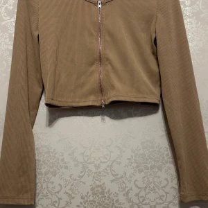 Beige croppad tröja - Säljer en beige croppad top med dragkedja framtill. Toppen har långa ärmar och är perfekt för höst och vår. Den är i nyskick och passar bra till både vardag och fest.