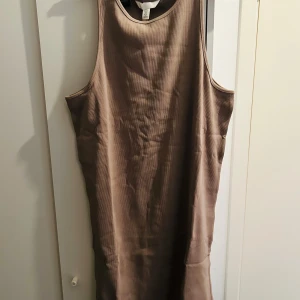 Beige ärmlös klänning - Säljer en stilren beige ärmlös klänning i ribbat material. Perfekt för en avslappnad sommarlook eller att styla med accessoarer för en festligare känsla. Klänningen har en enkel och bekväm passform.
