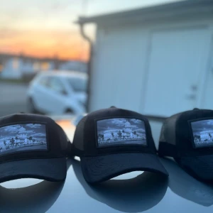 Svart velvet keps - Säljer en svart keps med ett  tryck av en byggnad på framsidan. Kepsen har ett nätmaterial på sidorna och baksidan för bra ventilation. Materialet är velvet, märket är conté