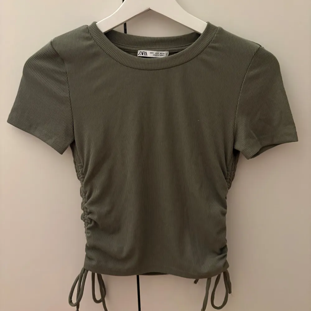 Snygg grön ribbad topp från Zara i mycket bra skick. Den har korta ärmar och en cool snörningsdetalj på sidorna som ger en fin passform. . Yläosat.