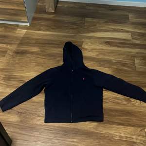 Säljer en svart hoodie från Polo Ralph Lauren i storlek 14-16 . Den har en dragkedja framtill och är perfekt för både höst och vinter. Hoodien är i bra skick och har en klassisk design med en liten logga på bröstet. Nypris: 1200kr